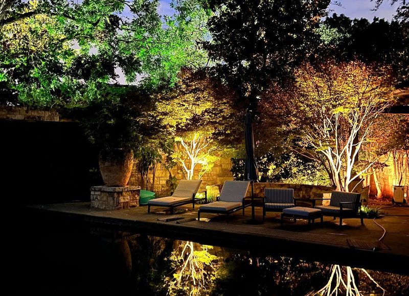 Landscape lighting illuminating trees and a patio at dusk