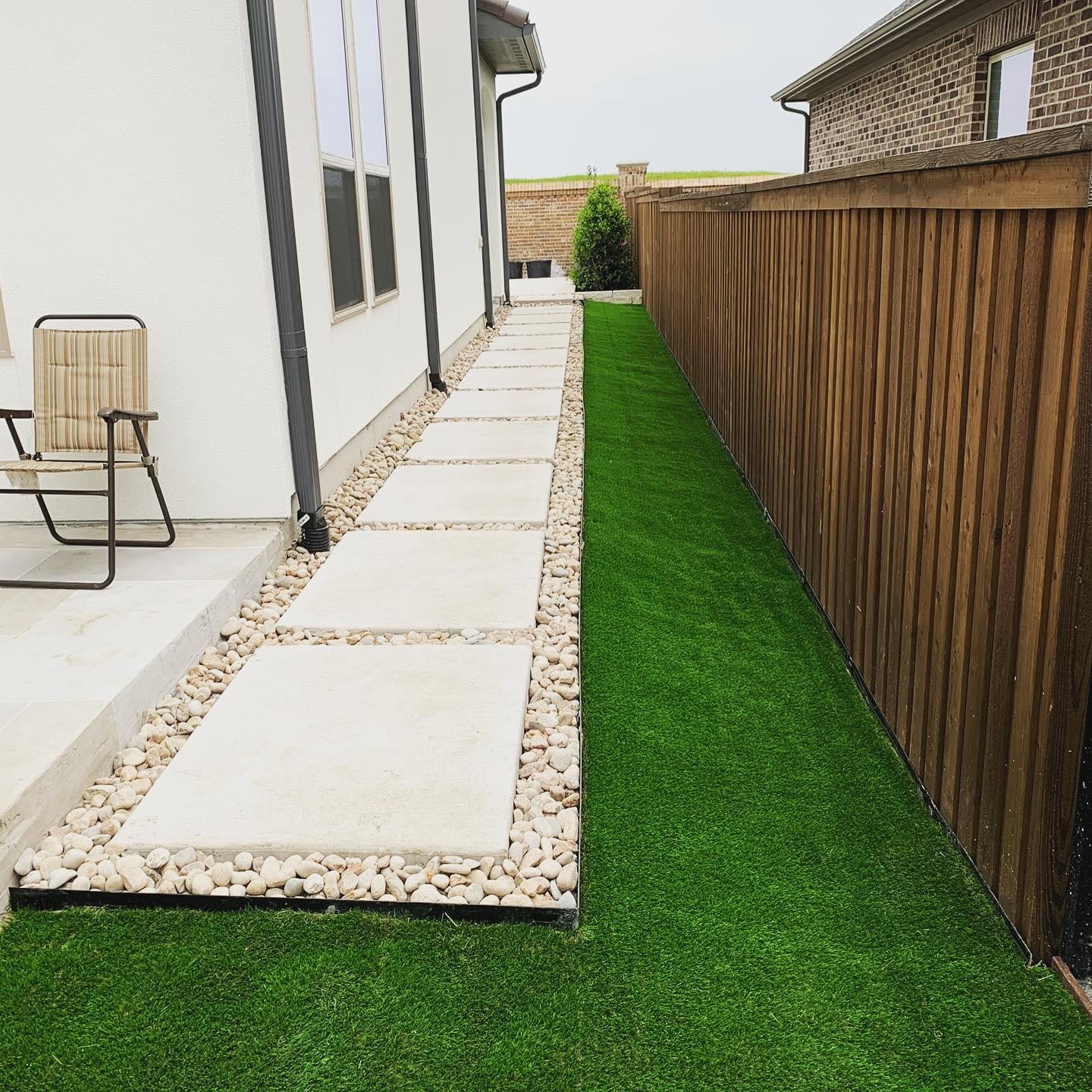 Side yard drainage channel with river rock and paver stepping stones beside artificial turf