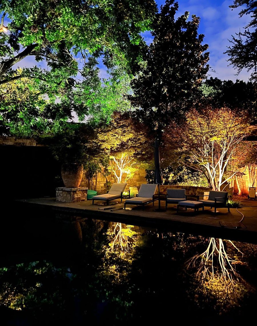 Professional landscape lighting illuminating trees and a patio at dusk